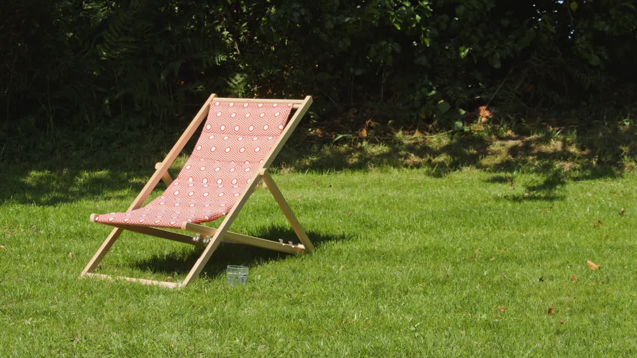 Sunlounger on green grass in vibrant garden, handheld view