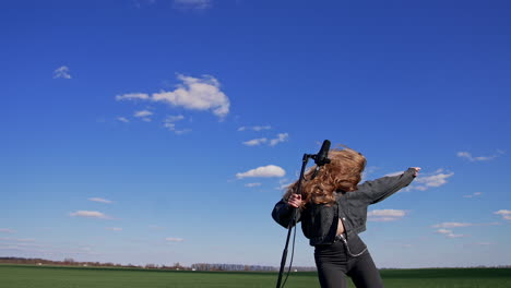 young rock star dancing near microphone outdoors. beautiful long-haired girl singing and moving her head with fluttering hair on blue sky background.
