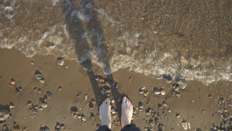 sea waves splashing to a woman's feet standing on the stony shore - top shot