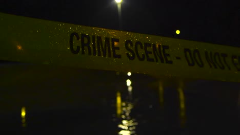 yellow crime scene do not enter police caution ribbon tape close up pulled in front of a dark night skatepark where heavy rain is falling. the tape is lit from the back by bokeh blurry street lights