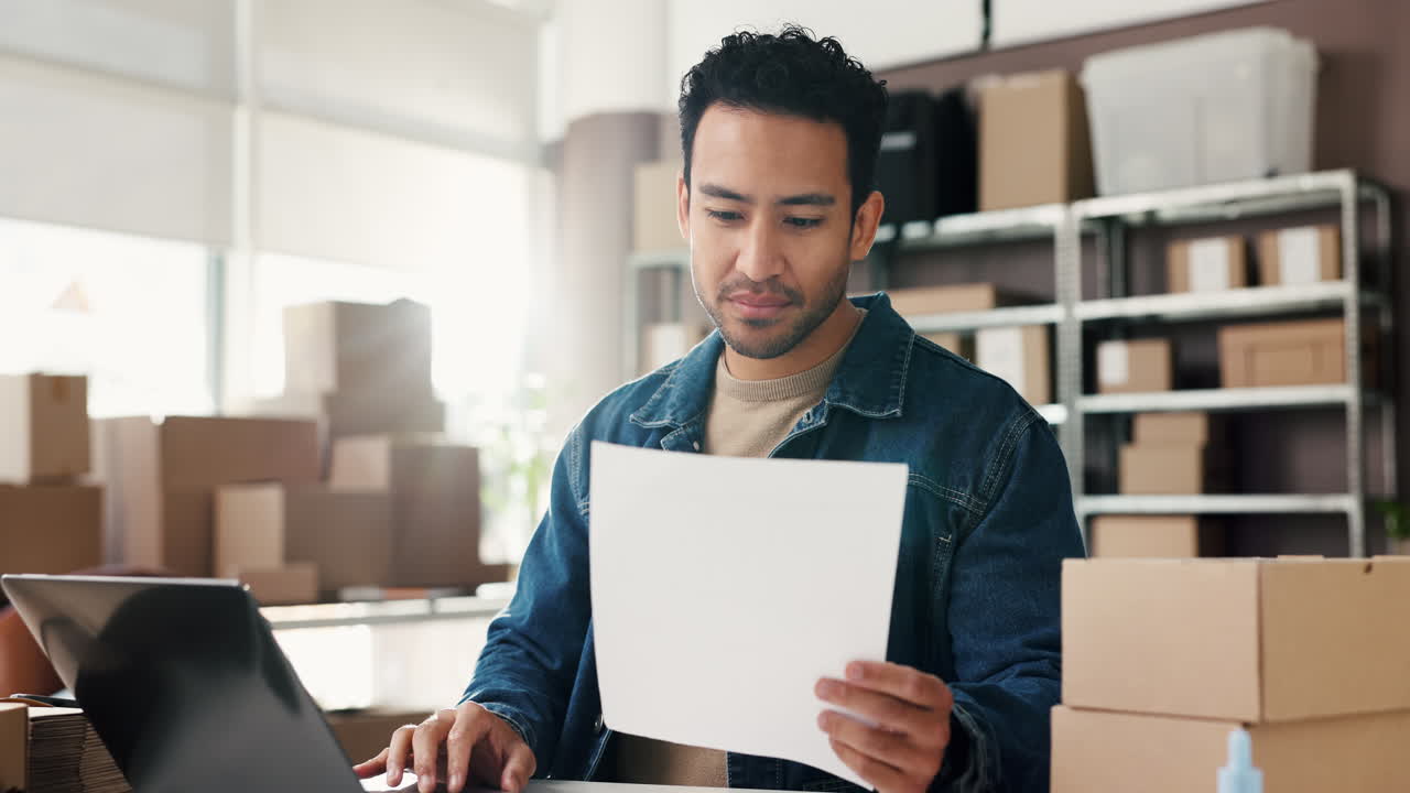 Young Man Working on Laptop and Checking Documents in E-commerce Office