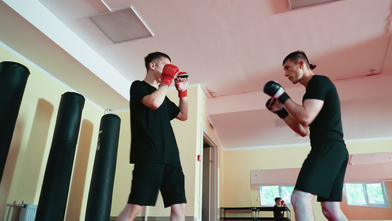 Fighters with boxing gloves sparring indoors on red mat in martial arts gym, practicing combat techniques, defense, and attack stances with intensity, focus, and physical energy during training session