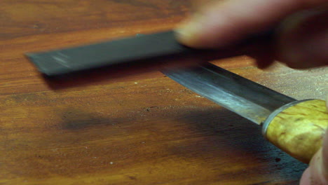 man hones sharp edge of forged knife, countertop close up view