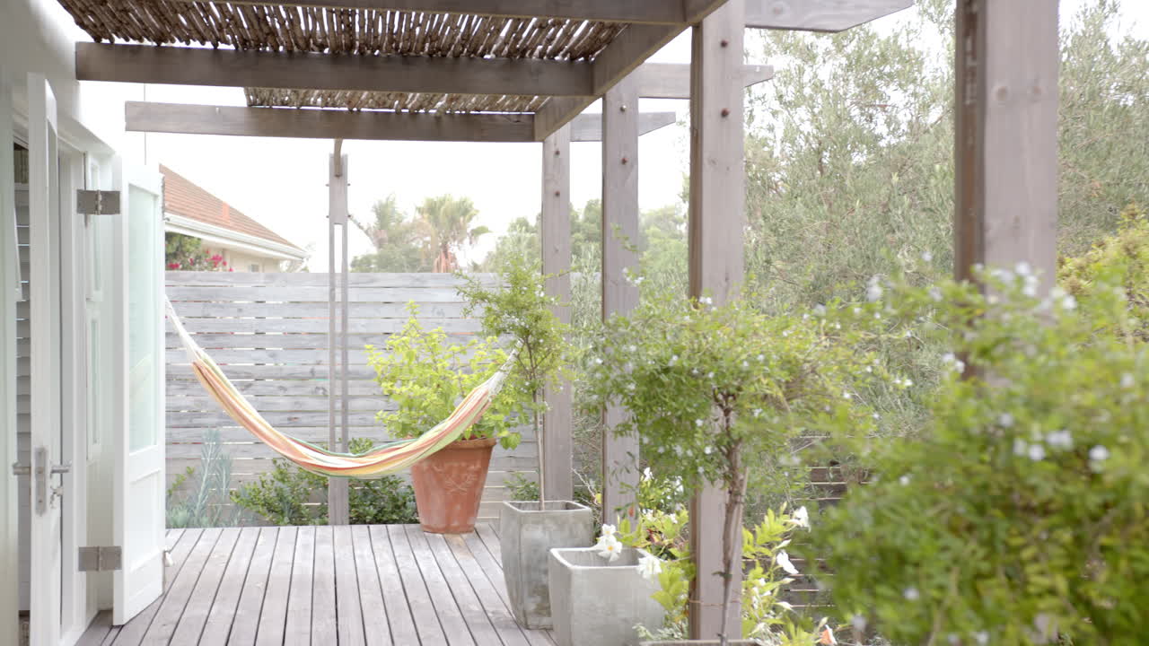 Empty hammock hanging on wooden deck in peaceful backyard garden, copy space