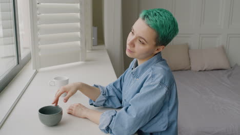 smiling young woman standing close to the window in the bedroom while her boyfriend approaching and kissing her