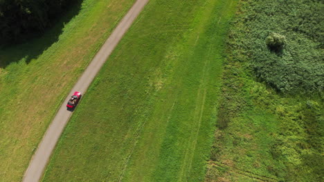 top-down view of a red convertible car driving on the road surrounded by the lush green meadow and field on a sunny day in zwolle, netherlands