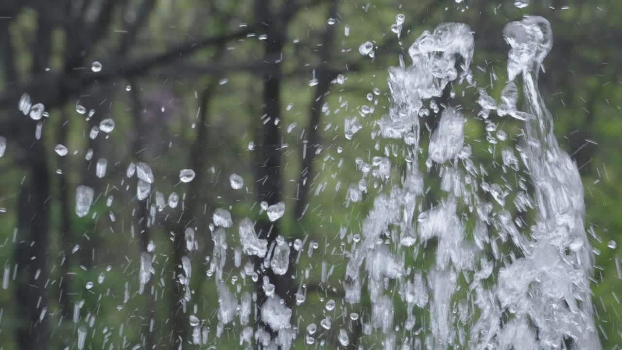 Splashing bubbling clear fountain water against park tree greenery outside