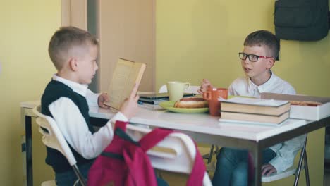 schoolboy-reads-book-to-friend-eating-at-table-in-canteen