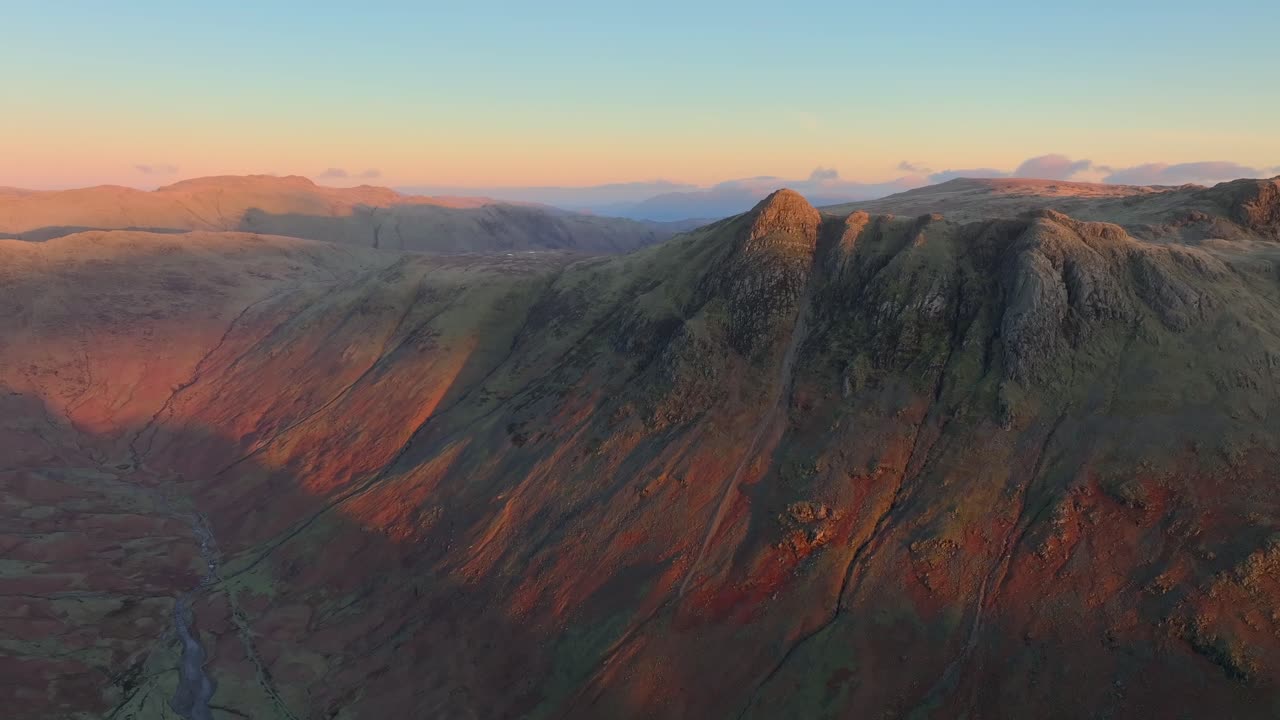 Dawn light striking mountains, pikes and fells with deep valley and clear skies. Slow panning shot. Langdale Pikes, English Lake District, Cumbria, UK.