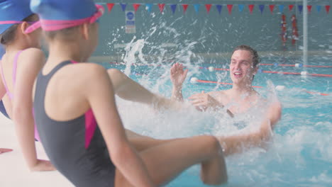 niños salpicando entrenador masculino en clase de natación mientras se sientan en el borde de la piscina cubierta