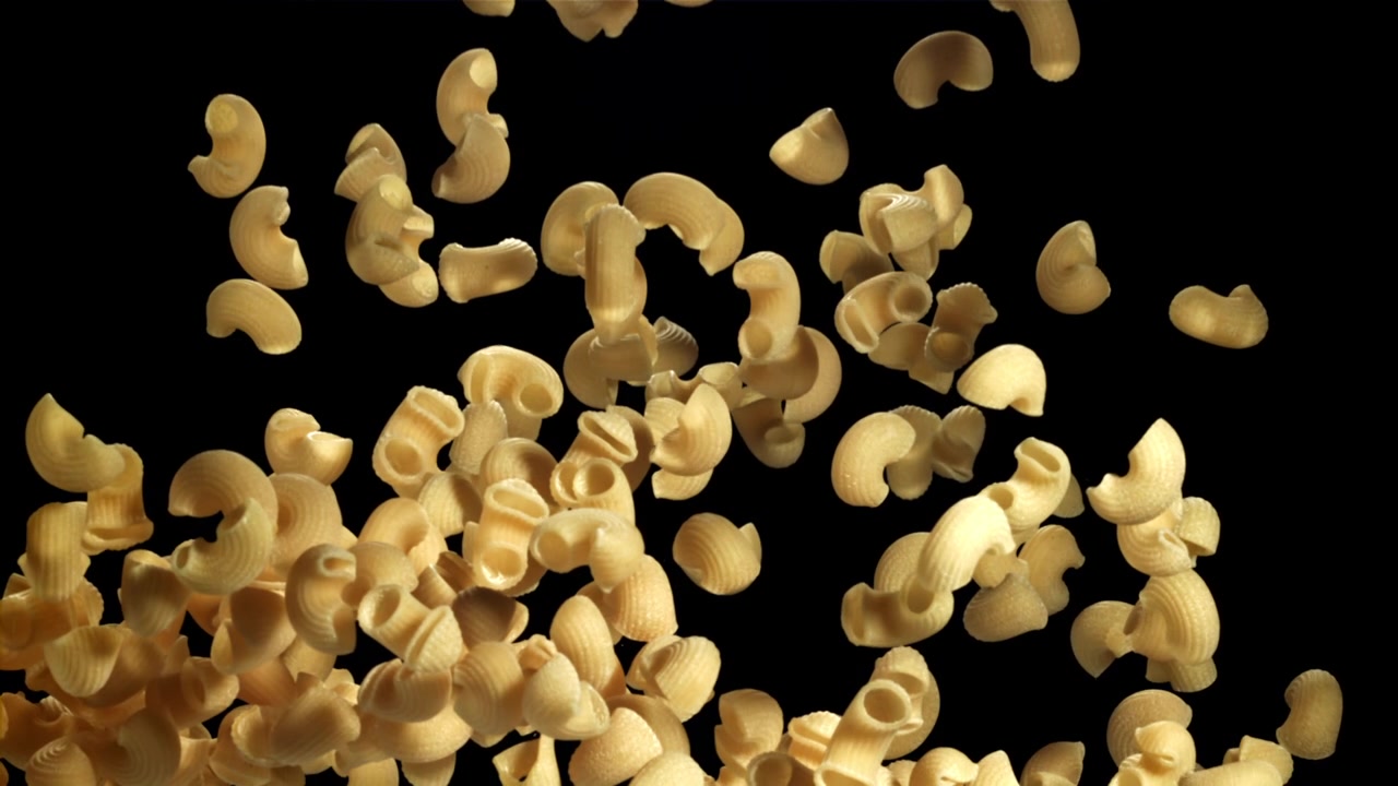Pasta maccheroni secca che cade al rallentatore su sfondo nero.
