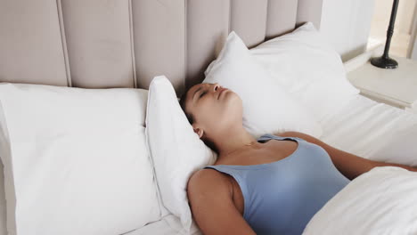 mujer biracial cansada acostada en la cama cubriendo la cara en casa, cámara lenta