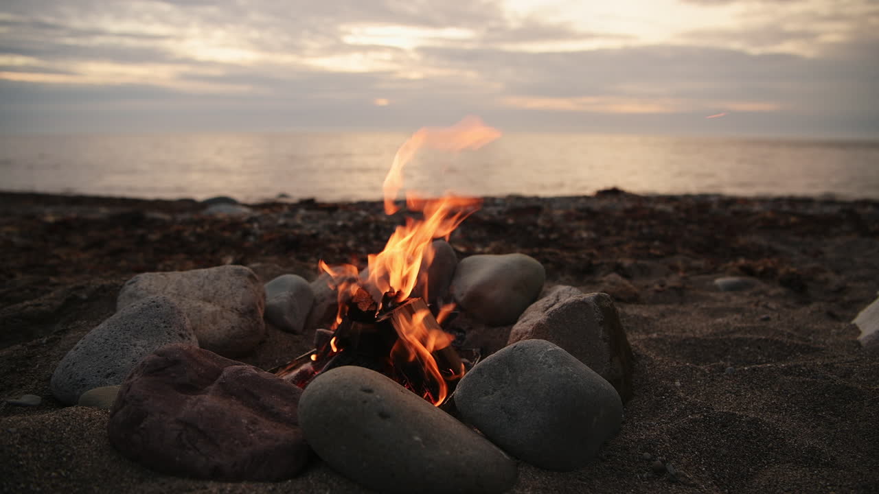 Wild camping on the beach - Small campfire bonfire surrounded by rocks on shore in Wales during outdoor adventure camping trip