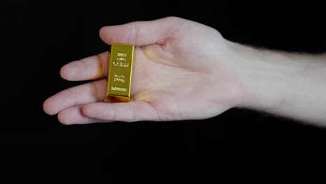person replaces gold bar in hand with one bitcoin, concept of exchanging physical for digital, black background.