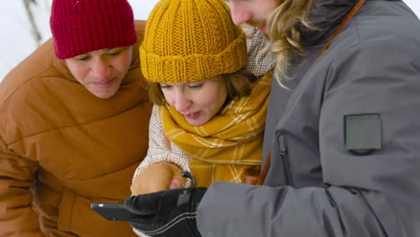 three friends in winter clothes looking at smartphone and laughing