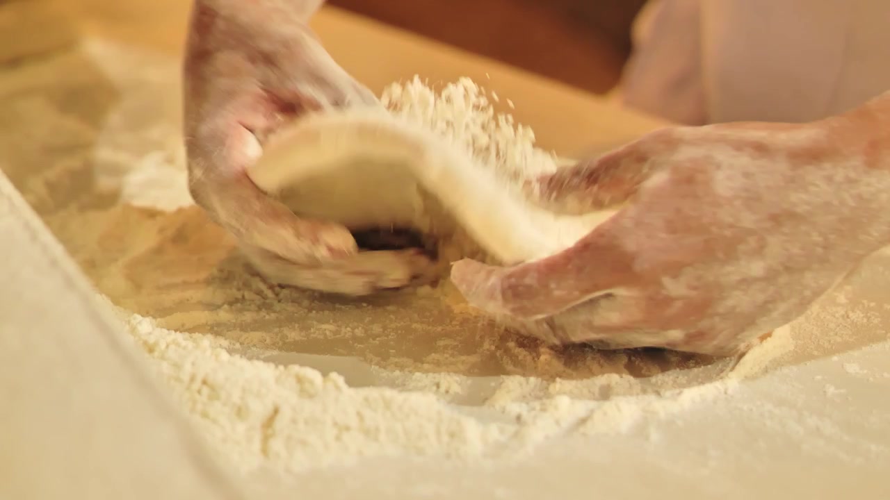 Kokki vaivaa tuoretta pizzataikinaa käsin jauhotetulla työtasolla.
