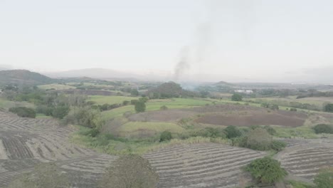 Aerial-drone-shot-in-slow-motion-approaching-a-mild-forest-fire-on-a-hill-on-a-cloudy-day,-smoke-poised-to-erupt-into-flames