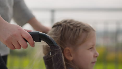 Hands-of-caring-woman-pushing-wheelchair-with-little-girl