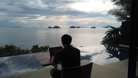 asian man working on the laptop by the pool - back view