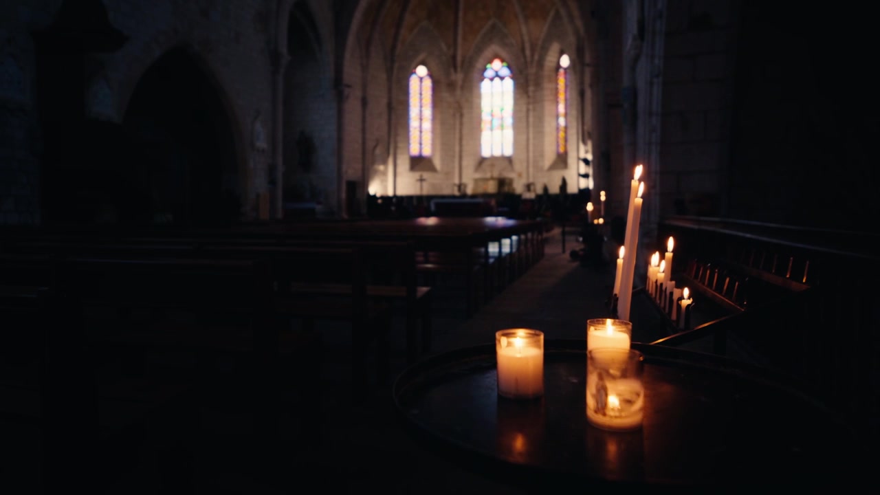 Brændende stearinlys på et bord i det mørke gotiske interiør af Saint-Dominique kirken i Monpazier, Dordogne. Slowmotion kørende optagelse