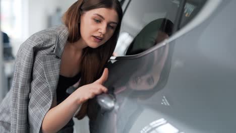 primer plano de una mujer joven inspeccionando la pintura de un automóvil