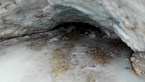 Aerial-flyover-away-from-the-ice-cave-of-the-Zinal-glacier-in-Valais,-Switzerland-with-a-pan-up-view-from-the-melting-glacial-water-stream-up-to-the-alpine-valley