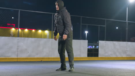 joven patea hábilmente la pelota en el campo deportivo urbano bajo las luces brillantes del estadio durante la sesión de práctica nocturna, el fondo presenta una valla metálica, un edificio residencial iluminado