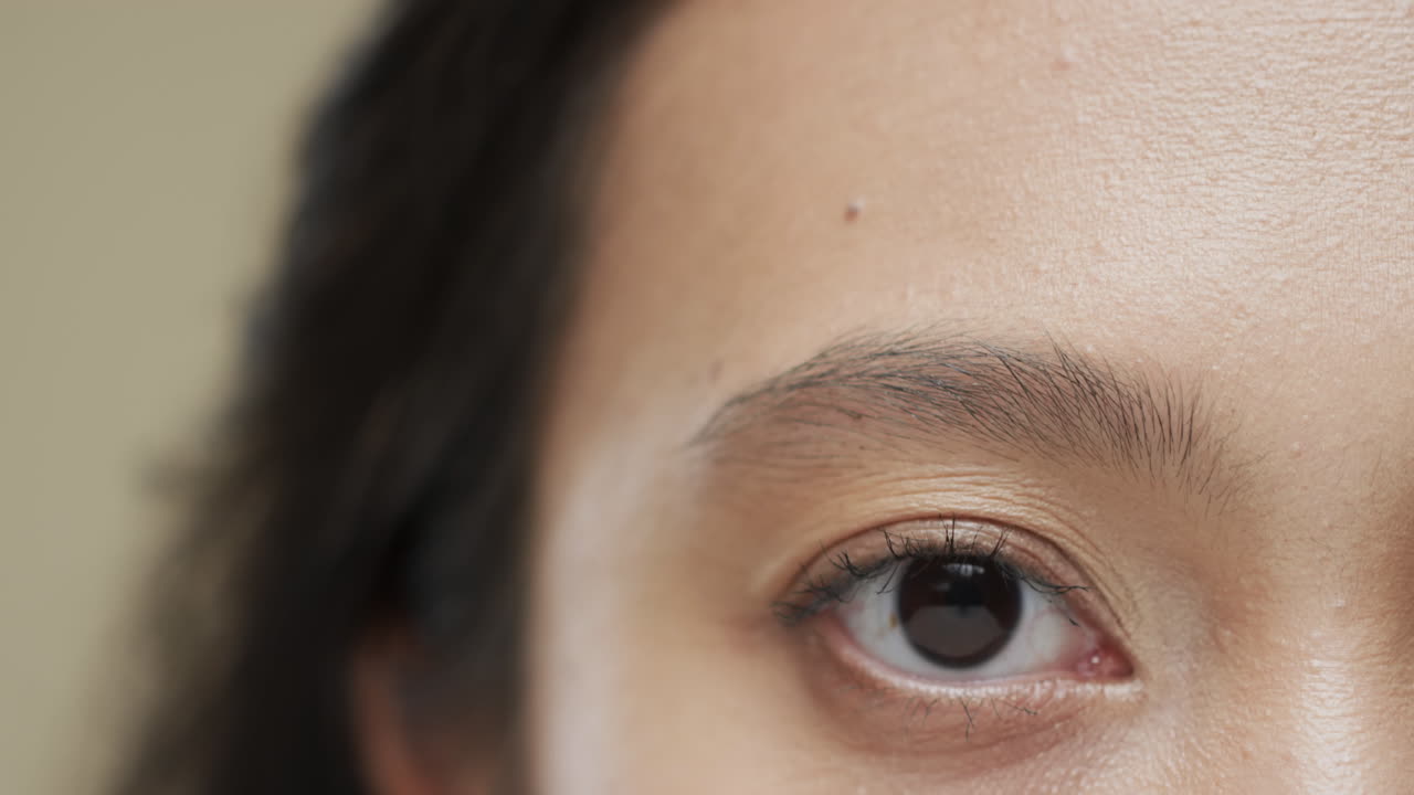 베이지색 배경에 어두운 머리카락을 가진 아시아 여성의 눈, 느린 동작
