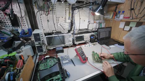 electronic equipment repair shop. the engineer technician solders the printed circuit board of an electronic device under a microscope.