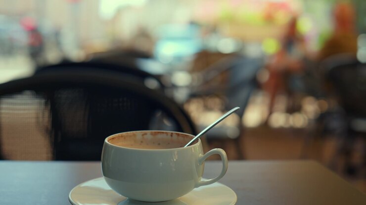 Empty white coffee cup with a spoon inside resting on a saucer at a blurred outdoor cafe table