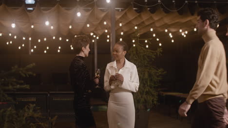 Two-Elegant-Multiethnic-Women-With-Champagne-Glass-Talking-To-Each-Other-And-Then-Welcoming-Two-Men-To-New-Year's-Eve-Party-1