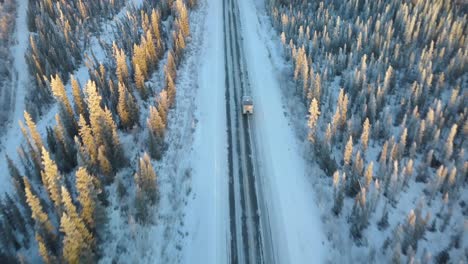 aerial, drone shot, following a work truck on a the alaskan highway, surrounded by frosty woods, during sunset, in alaska, united states