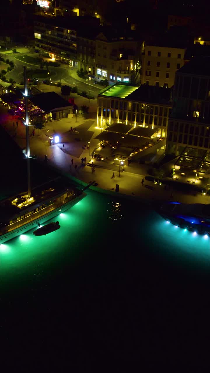 Vertical aerial night shot of Split’s harbour, featuring yachts lit up along the waterfront