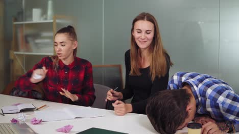 group of tired workers in a creative start up work environment holding a project meeting in a conference room. they are discussing a project and crumpling papers, working hard before the deadline