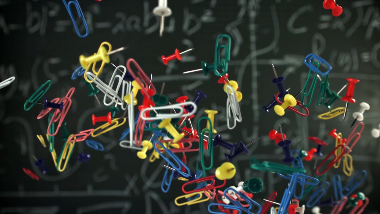 Colorful Paper Clips and Pushpins Falling in Slow Motion Against a Chalkboard