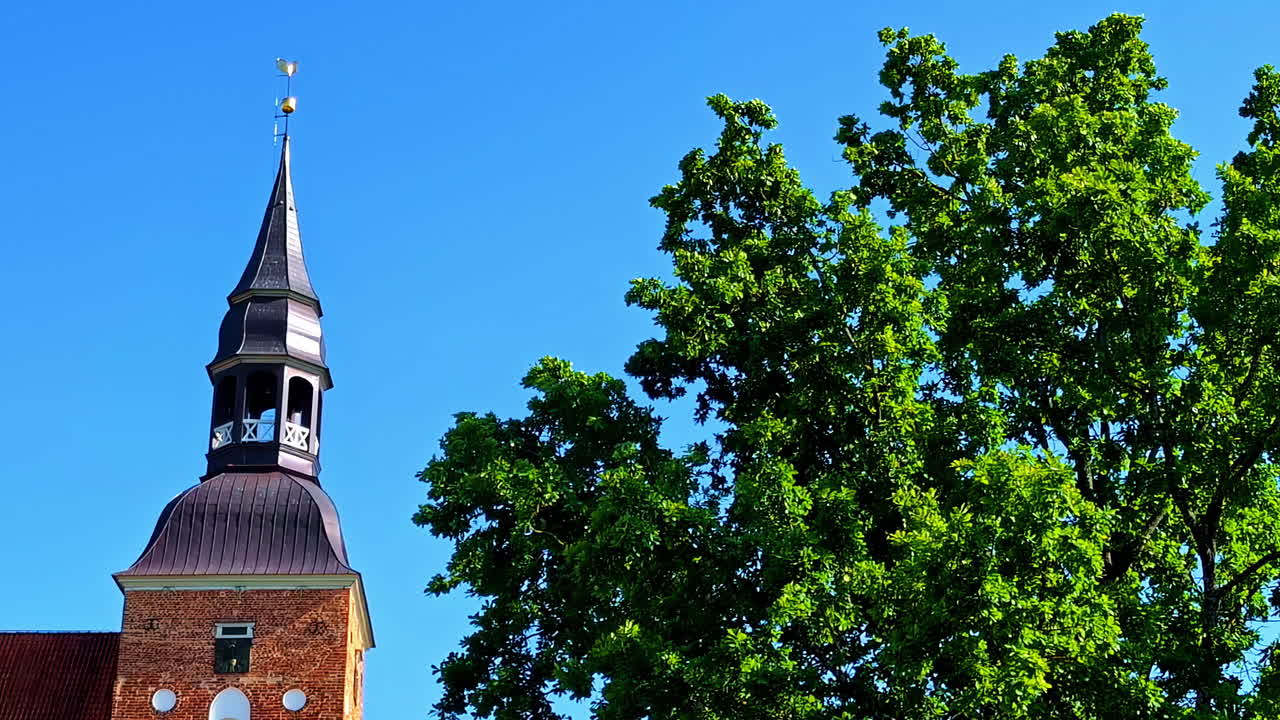 Church tower with spire and green tree against clear blue sky in summer