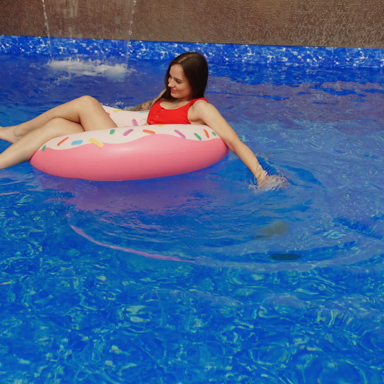 Long-haired girl in a swimming suit like a bagel enjoying sun. Young lady spending time in a pool outdoors