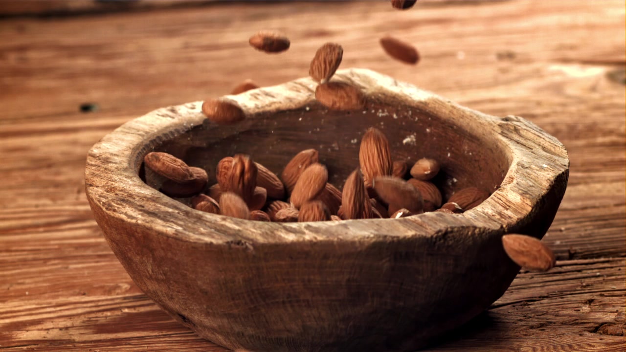 Mandorle che cadono al rallentatore in una ciotola di legno rustica.