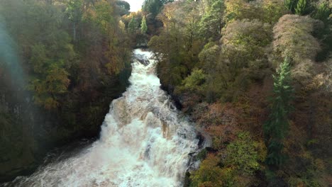 Slowly-reversing-drone-footage-of-a-cascading-waterfall-in-a-gorge-surrounded-by-colourful-trees-in-autumn