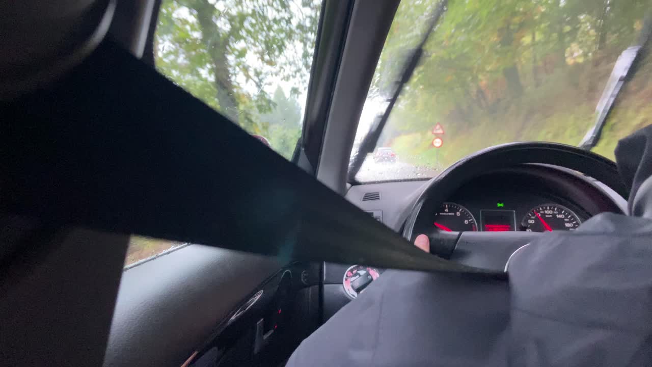 vista sobre el hombro detrás de la persona que conduce el automóvil a través de la lluvia con los limpiaparabrisas encendidos