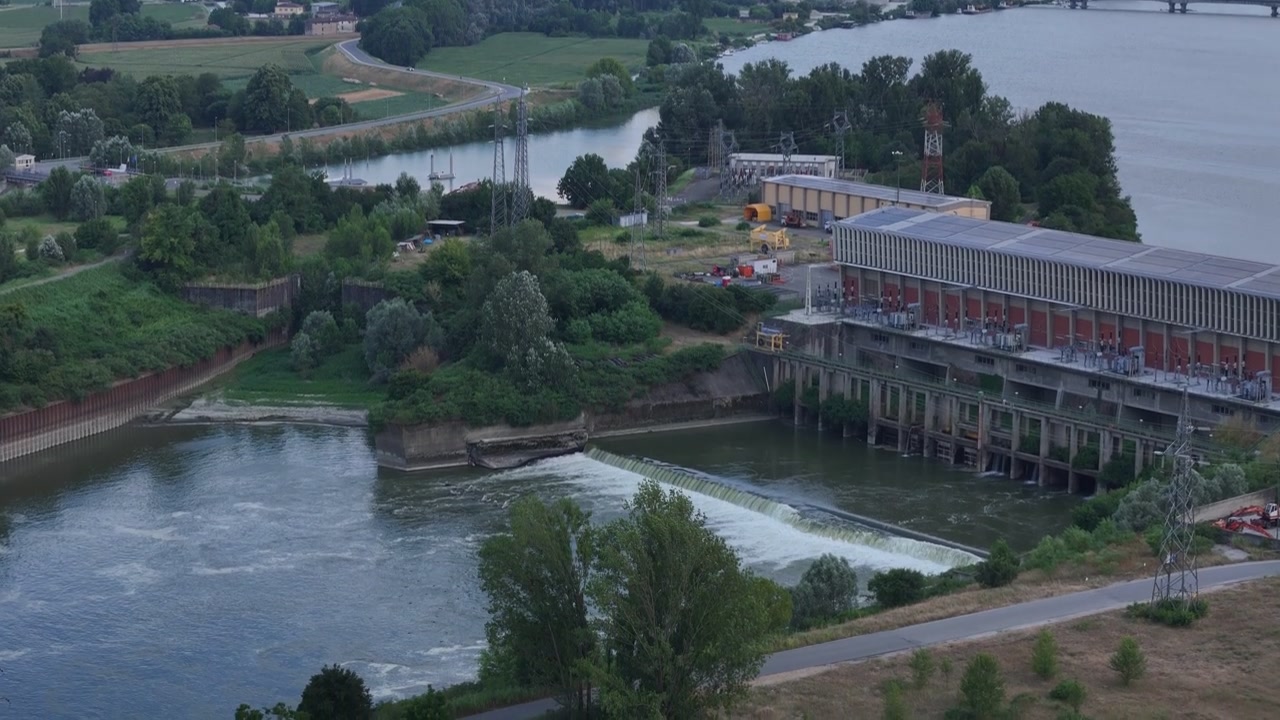 Přehrada Isola Serafini na řece Pád u Monticelli d'Ongina, Piacenza, Emilia-Romagna, Itálie, ukazující hydroelektrárnu, rybí propust, jez a krajinu záplavové oblasti, záběr dronem vpřed.
