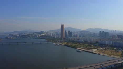 drone shot traveling forward above the han river toward the mapo bridge and a business district with skyscrapers in seoul city during the day