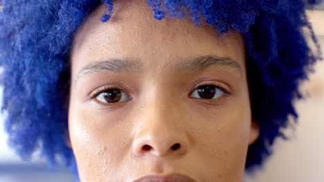 portrait close up of happy biracial creative businesswoman with blue afro smiling, in slow motion