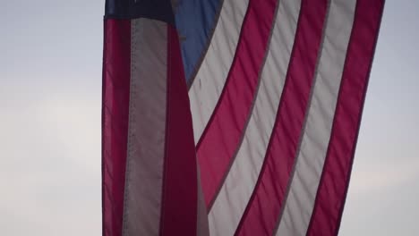 a close up shot of the american flag in slow motion. the flag is infront of a pretty sunset