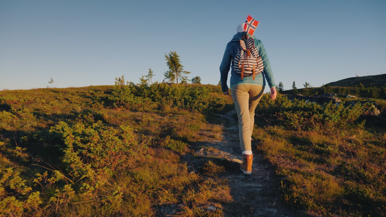 un turista con una bandera noruega en una mochila camina por las pintorescas tierras altas al amanecer activo