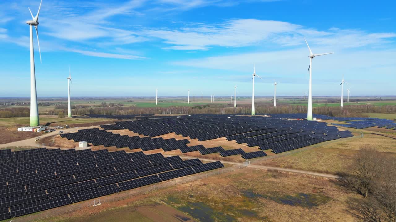 Aerial footage of solar panels plant and wind turbines a generating green electric energy on a wide green field on a sunny day, in Taurage, Lithuania