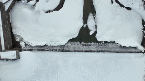 frozen dam with water flowing over, aerial winter landscape with icy river and snow