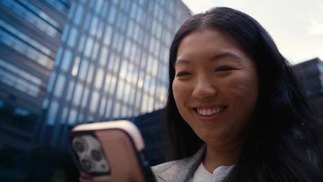 Low-angle-view-of-cheerful-business-Chinese-woman-browsing-mobile-phone