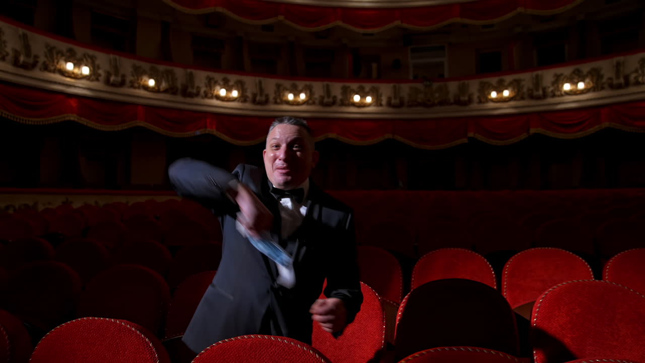 Happy actor puts off medical mask and throws it. Man in costume sitting in the empty theatrical hall and invites joyfully to come to performance. The end of pandemic.
