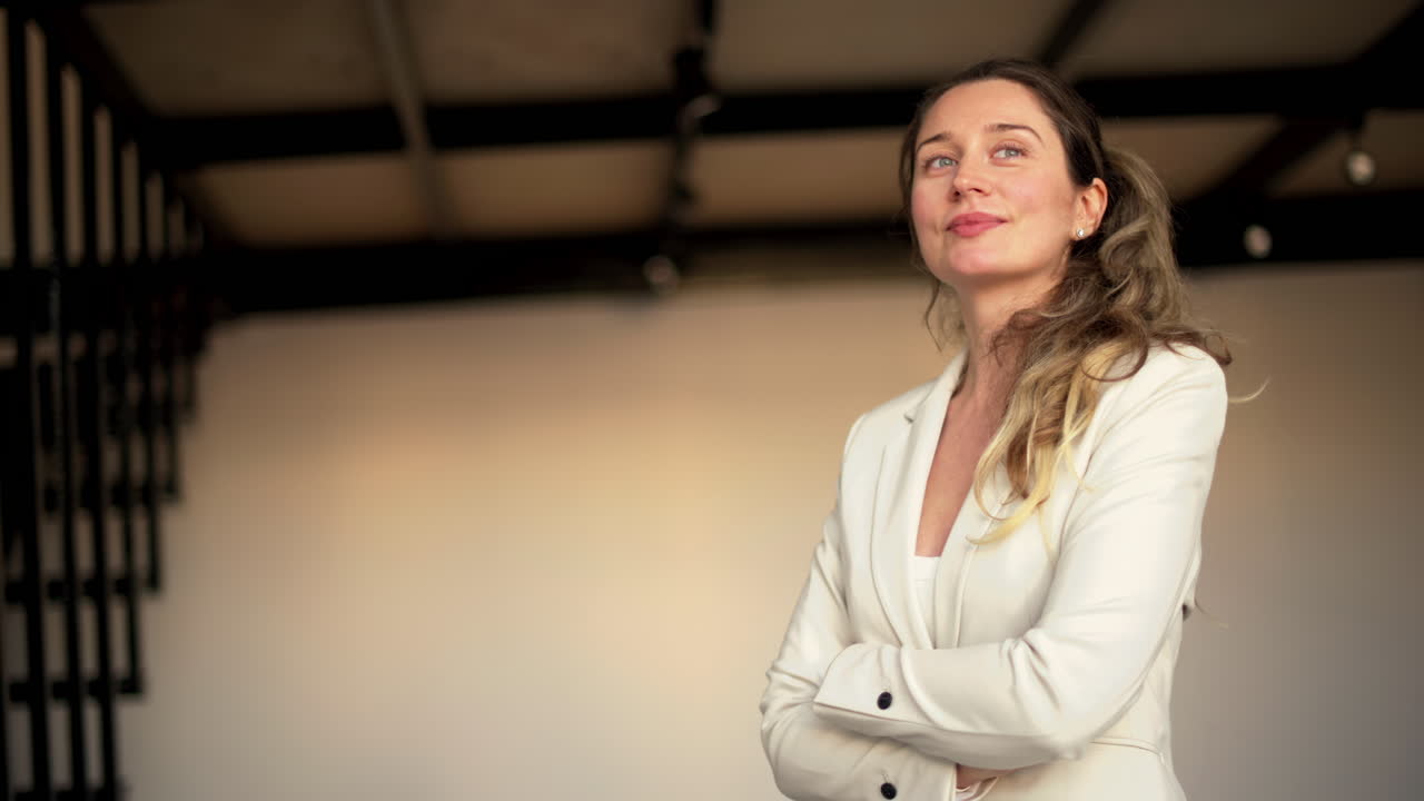 A professional woman in a white blazer standing confidently with crossed arms, conveying leadership and determination